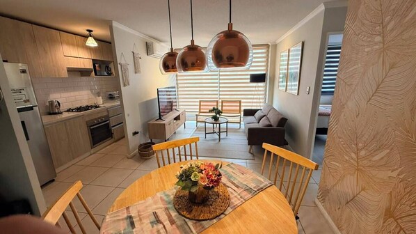 A modern kitchen with wooden cabinets, a dining table with a centerpiece, and pendant lighting.