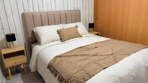 A neatly made bed with a beige headboard, two bedside tables with lamps, and a wooden door in the background.