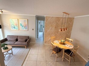 A living room with a sofa, a dining table with chairs, and a small round table with a plant.