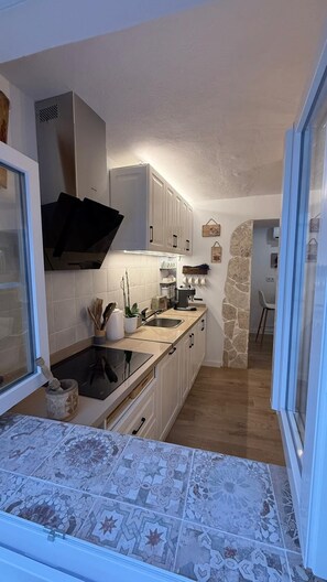 A compact kitchen with white cabinets, a black stove, and a stone accent wall. - Mama's House, where tradition and comfort will make you feel right at home (Mijas)