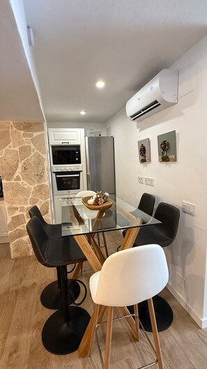 Een moderne keuken met een glazen eettafel, zwart-witte stoelen en een accentmuur van steen.