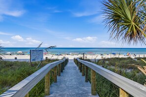 A wooden boardwalk leading to a beach with a signboard, sandy beach, and clear blue sky. - Gulf Highlands with a Golf Cart! (Panama City Beach)
