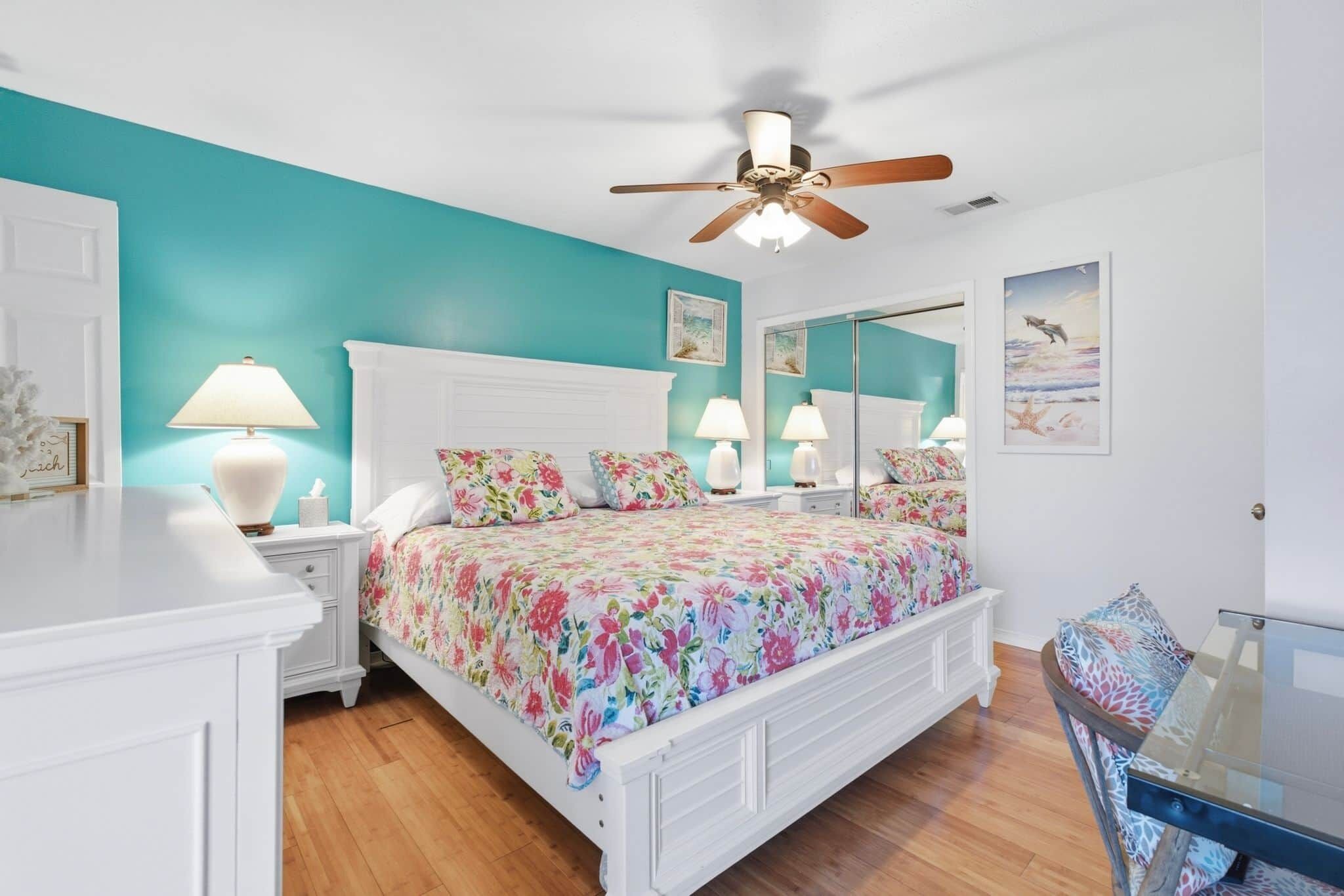 A bedroom with a bed, bedside tables, a ceiling fan, and a mirror.