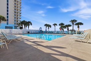 A pool area with lounge chairs and palm trees. - Gulf Highlands with a Golf Cart! (Panama City Beach)