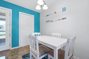 A dining area with a white table and chairs, a blue accent wall, and a door. - Gulf Highlands with a Golf Cart! (Panama City Beach)