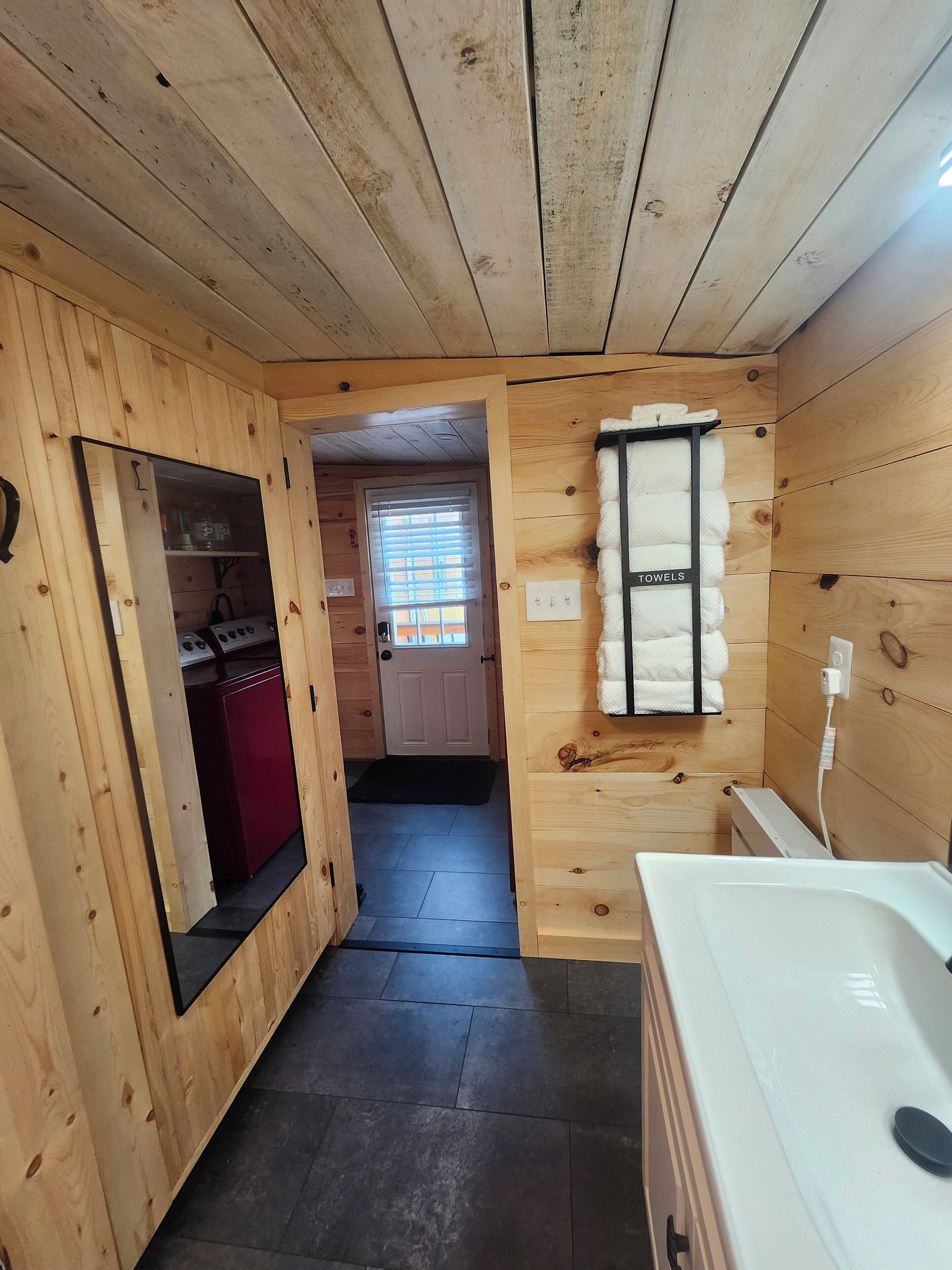 A wooden-paneled room with a mirror, a red cabinet, a towel rack, and a white bathtub.
