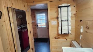 A wooden-paneled room with a mirror, a red cabinet, a towel rack, and a white bathtub.