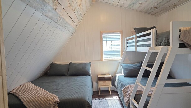 A loft bedroom with a sloped ceiling, two bunk beds, a small window, and a wooden floor.
