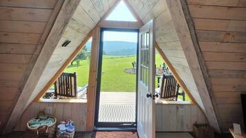 Une chambre mansardée avec un plafond en pente en bois, une porte donnant sur un balcon et une vue sur un paysage verdoyant.