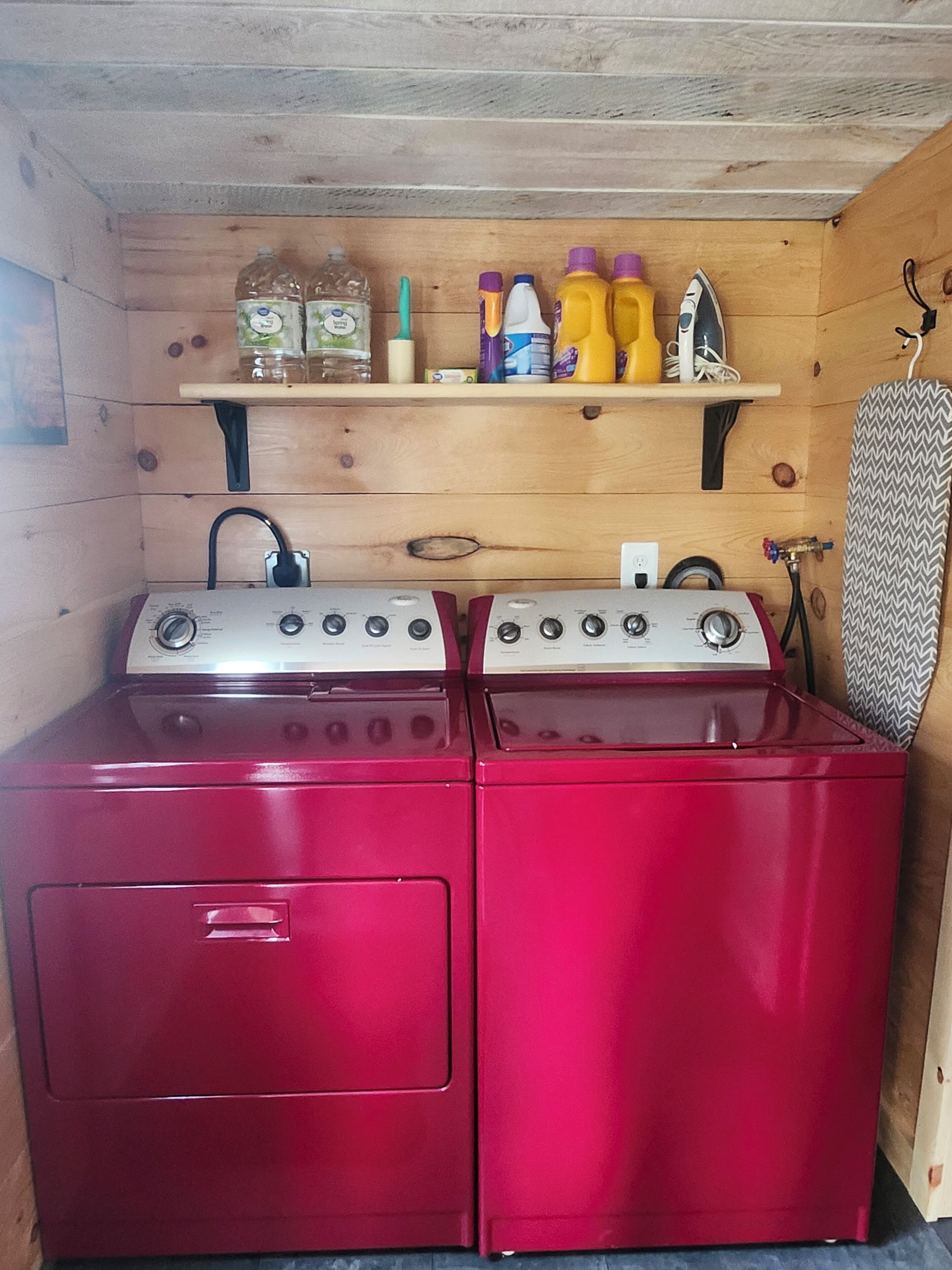 Une cuisine compacte avec un poêle et un four rouges, une étagère en bois au-dessus où sont rangés divers ustensiles de cuisine, et une serviette à motifs accrochée au mur.