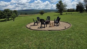 A circular seating area with chairs and a table, surrounded by a grassy field with trees in the background.