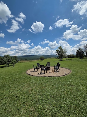 A circular seating area with chairs and a table, surrounded by a grassy field with trees in the background.