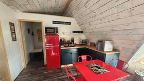 A compact kitchen with a red refrigerator, a microwave, and a toaster. There is a dining table with red chairs and a small rug.