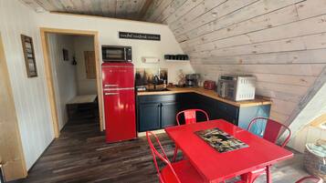 Cocina compacta con un refrigerador rojo, un microondas y un tostador. Hay una mesa de comedor con sillas rojas y una alfombra pequeña.