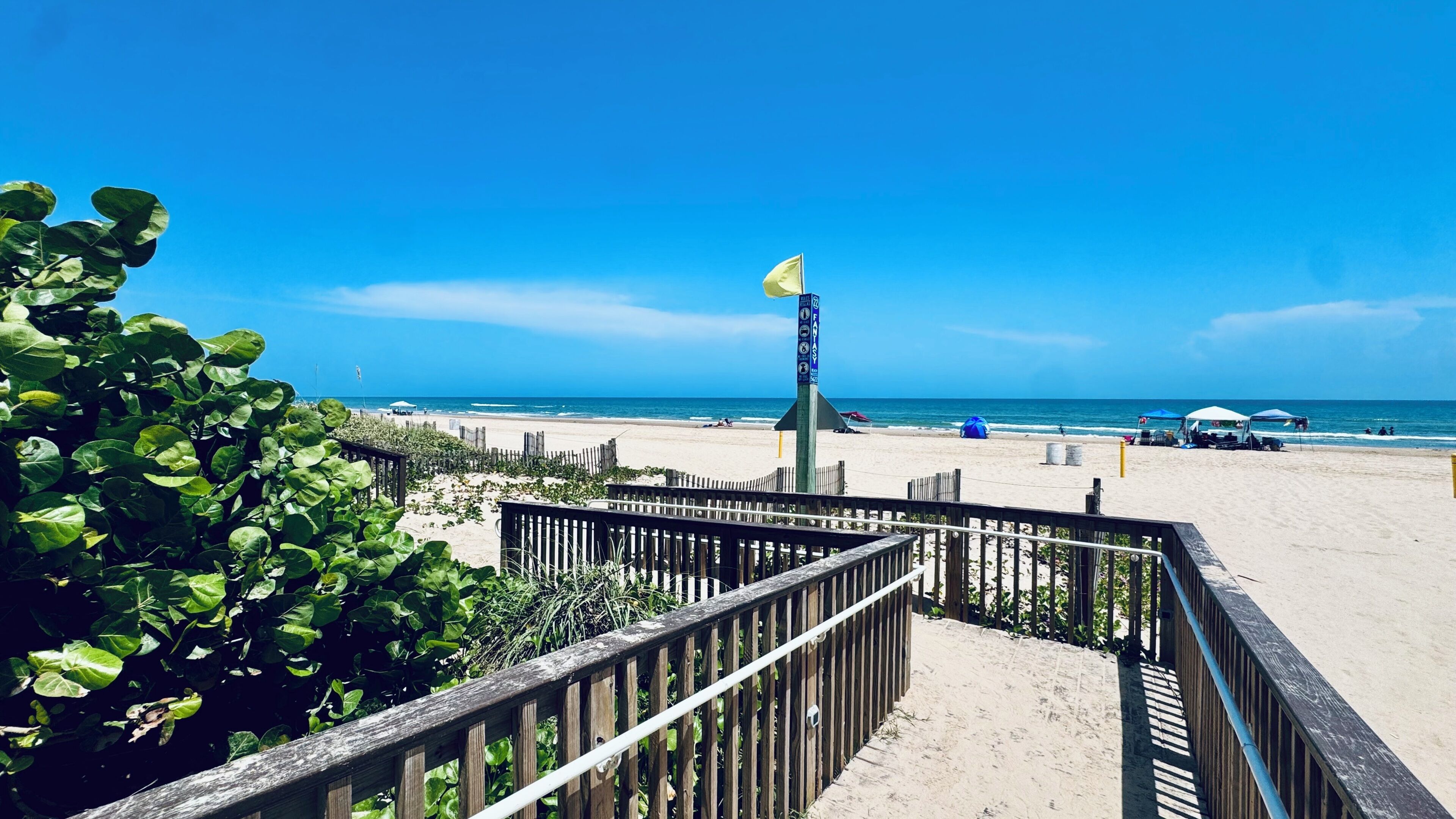 Una pasarela de madera que conduce a una playa arenosa bajo un cielo azul despejado.