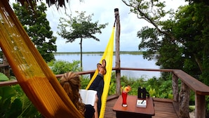 A hammock on a wooden deck overlooking a lake, with a table and binoculars nearby.