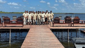 A group of people on a wooden dock with chairs and a covered area, overlooking a body of water.