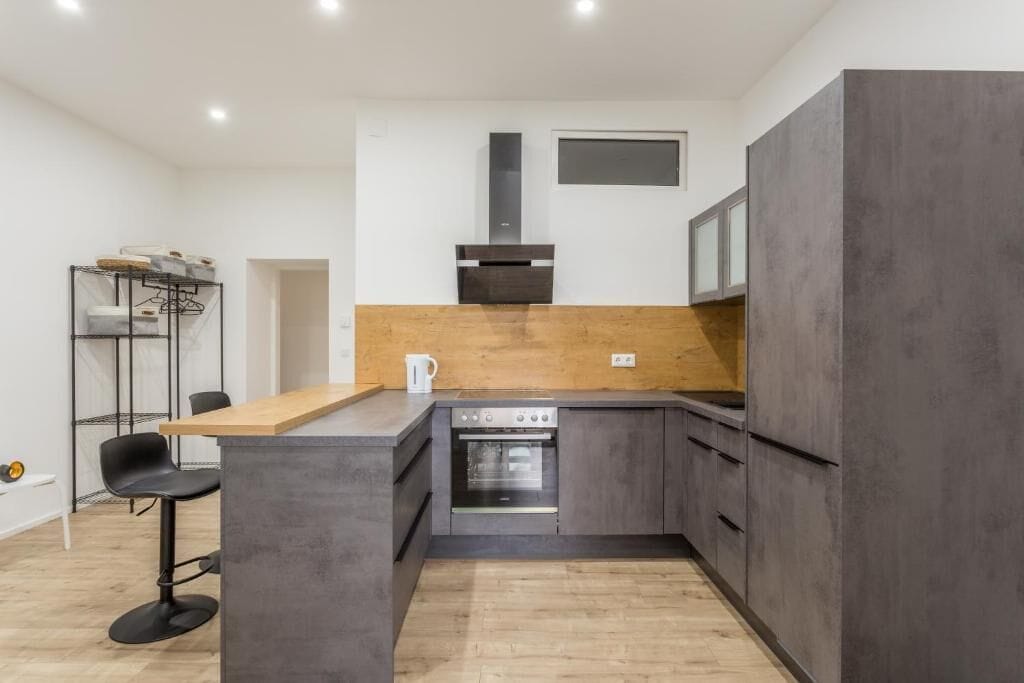 Eine kompakte Küche mit Einbauofen, Holz Arbeitsplatte und Barhocker.