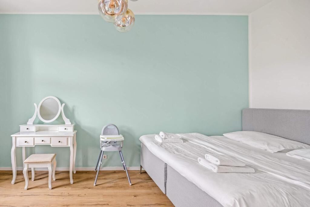 A bedroom with a bed, a vanity with a mirror, a small stool, and a ceiling light fixture.