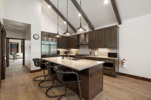 Una cocina moderna con una isla grande, taburetes de bar, electrodomésticos de acero inoxidable e iluminación colgante.