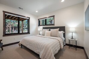 A bedroom with a bed, two bedside lamps, a window with a view, and a mirror on the wall. - Sierra Luxe Retreat - Hot tub close to Stateline (Zephyr Cove)