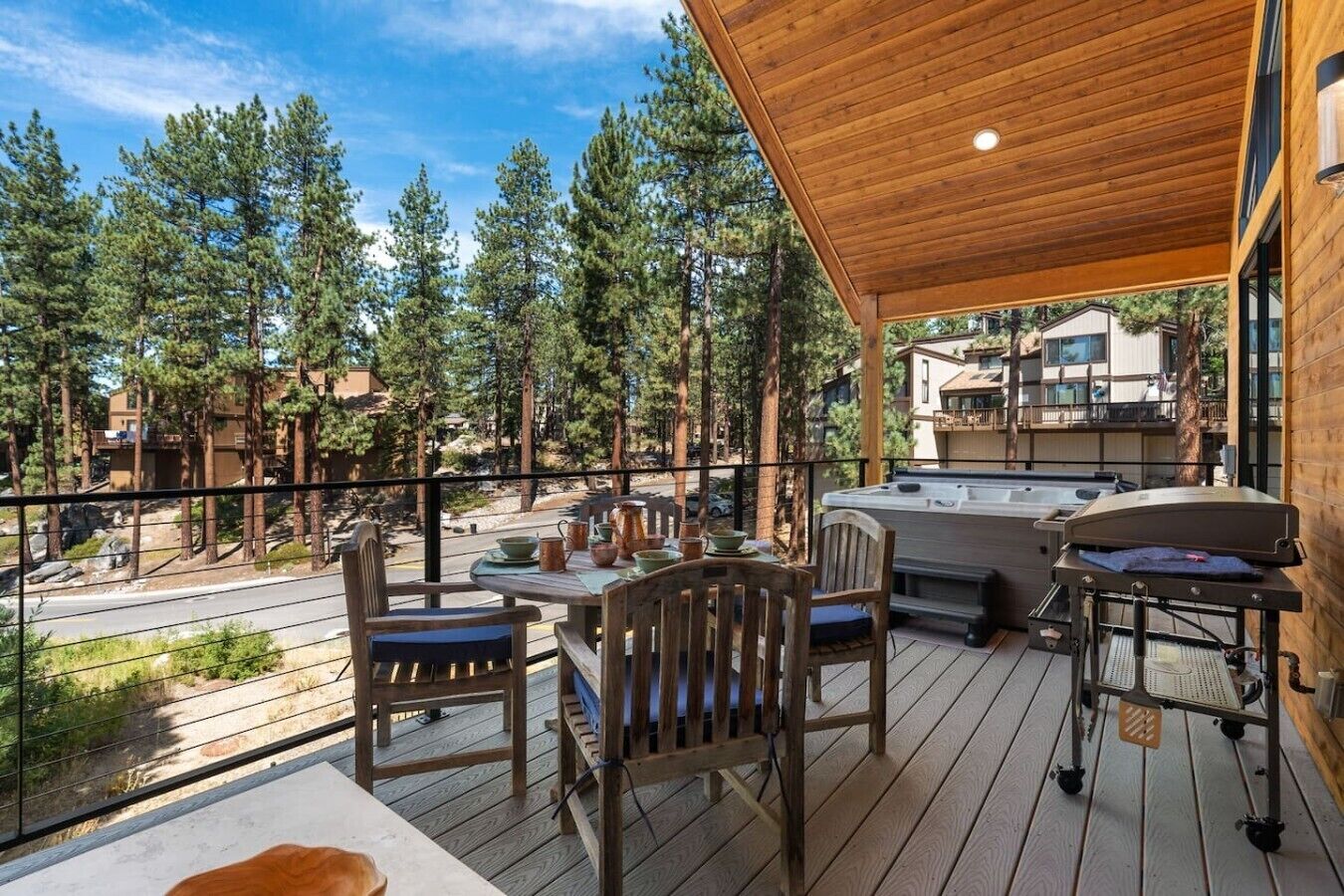 Una terraza de madera con mobiliario exterior, un jacuzzi y vistas a un área boscosa.
