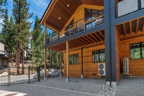 Une cabane en bois à deux étages, dotée d’un balcon, de grandes fenêtres et d’un appareil de climatisation.