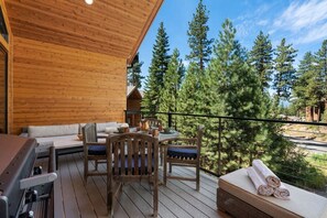 Une terrasse en bois avec une table et des chaises, un canapé et une petite structure en bois en arrière-plan.