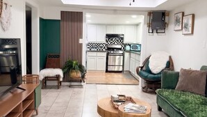 Una sala moderna con televisor, asientos y una cocina al fondo.