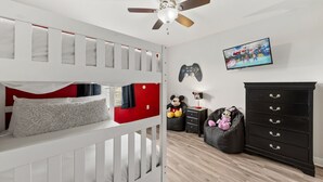 Ein Schlafzimmer mit Etagenbett, Deckenventilator, Spielkonsole, Fernseher und Kommode.