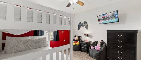 A bedroom with a bunk bed, a ceiling fan, a gaming console, a television, and a dresser.