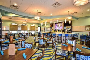 A hotel lobby with multiple dining tables, chairs, a bar area, and a television screen. - 1583 Moon Valley Drive (Davenport)