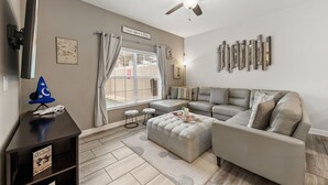 Ein Wohnzimmer mit einem grauen Ecksofa, einem Deckenventilator und einem flachbildfernseher, der an der Wand montiert ist.