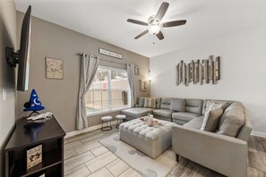 A living room with a grey sectional sofa, a ceiling fan, and a flat-screen TV mounted on the wall. - 1583 Moon Valley Drive (Davenport)