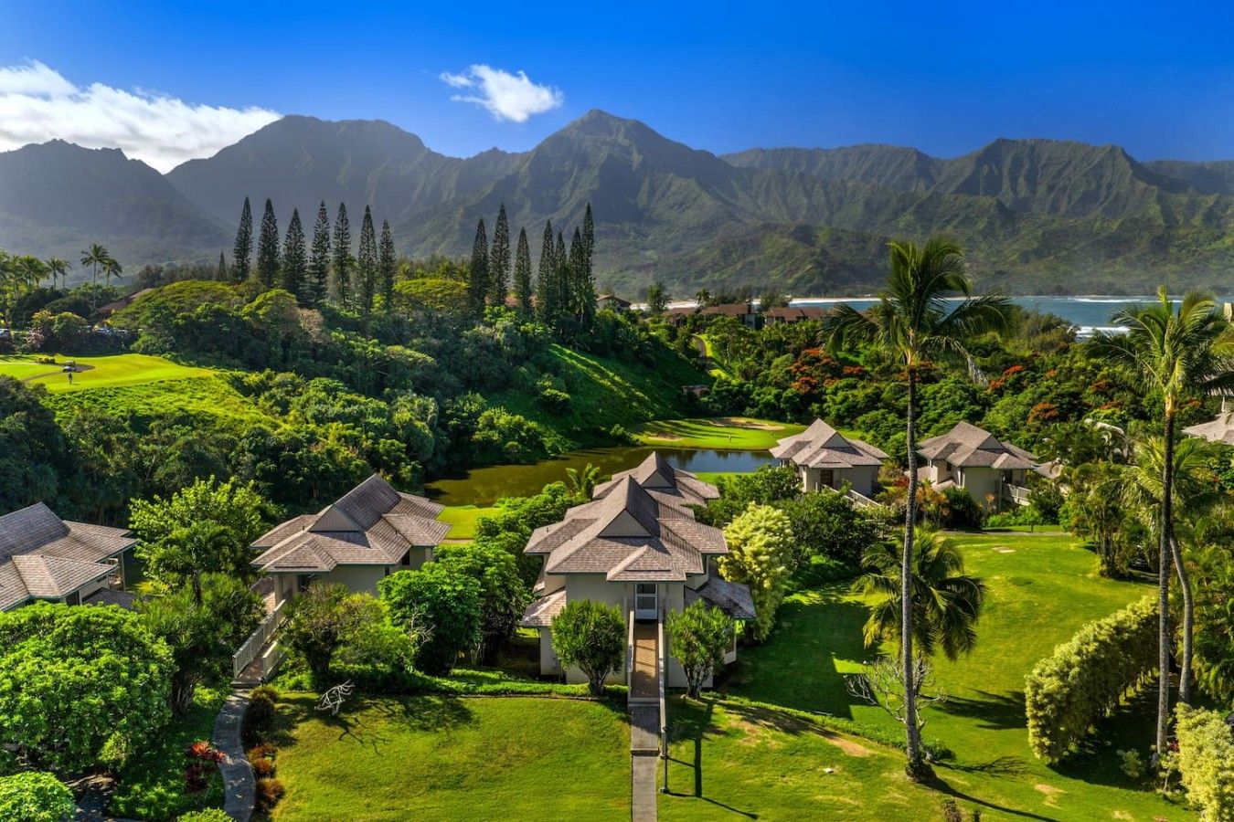 Un resort con varias edificaciones, un campo de golf y vistas a montañas y una masa de agua.