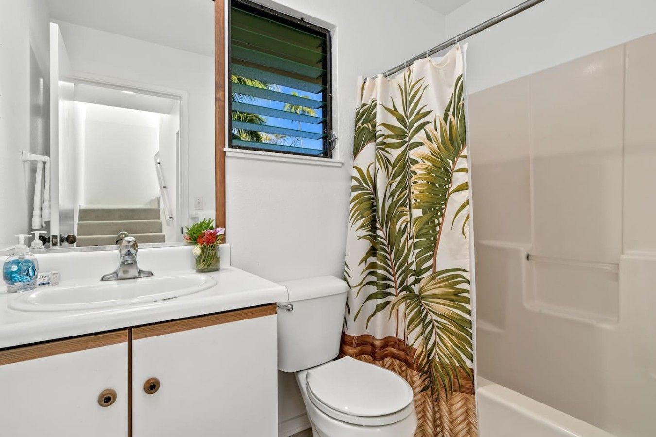 A bathroom with a white sink, a mirror, a toilet, and a shower curtain with a tropical leaf pattern.
