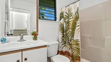 A bathroom with a white sink, a mirror, a toilet, and a shower curtain with a tropical leaf pattern.