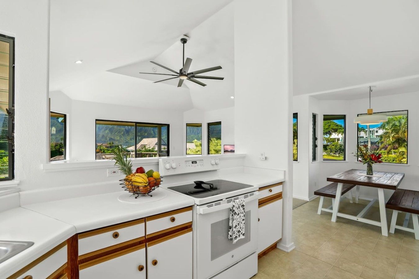 A modern kitchen with a central island, a ceiling fan, and large windows offering a view of the outdoors.