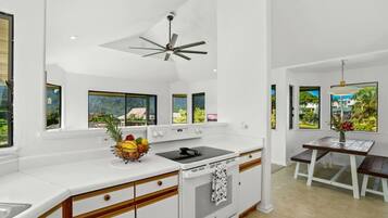 A modern kitchen with a central island, a ceiling fan, and large windows offering a view of the outdoors.