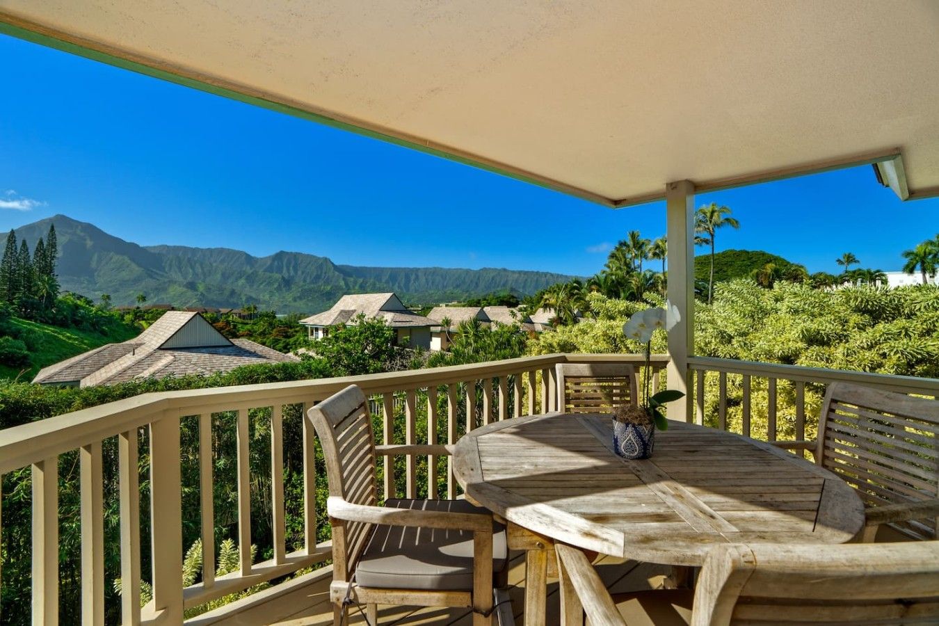 Une terrasse en bois avec une table et des chaises, offrant une vue sur un paysage montagneux parsemé de maisons.