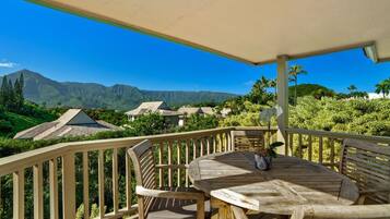 Une terrasse en bois avec une table et des chaises, offrant une vue sur un paysage montagneux parsemé de maisons.
