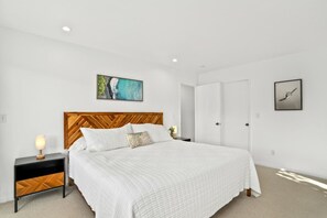 Une chambre à coucher avec un lit, une table de chevet, un tableau accroché au mur et une porte.