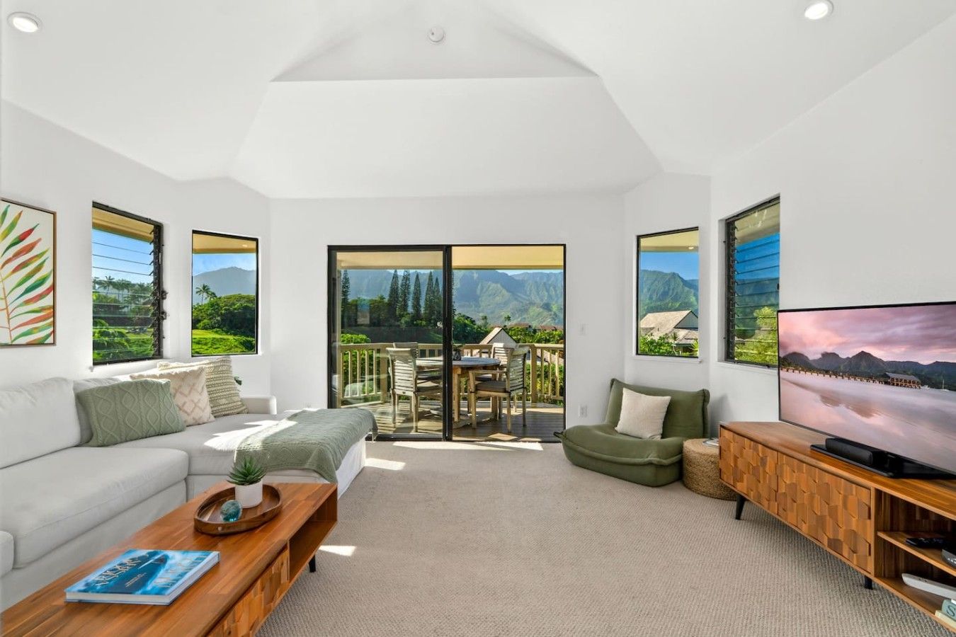 A spacious living room with a sofa, coffee table, and TV, featuring large windows with mountain views.