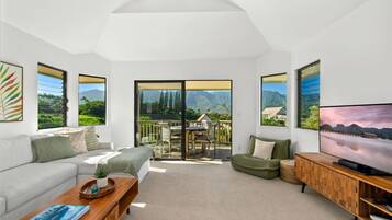 A spacious living room with a sofa, coffee table, and TV, featuring large windows with mountain views.