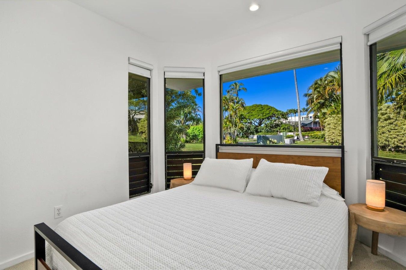 Quarto com uma cama grande, duas mesas de cabeceira e vista para um jardim tropical através de uma janela ampla.