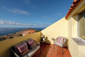 A balcony with a sofa and chair, a small table, and a view of the sea. - Ocean View Oasis House (Santa Cruz)