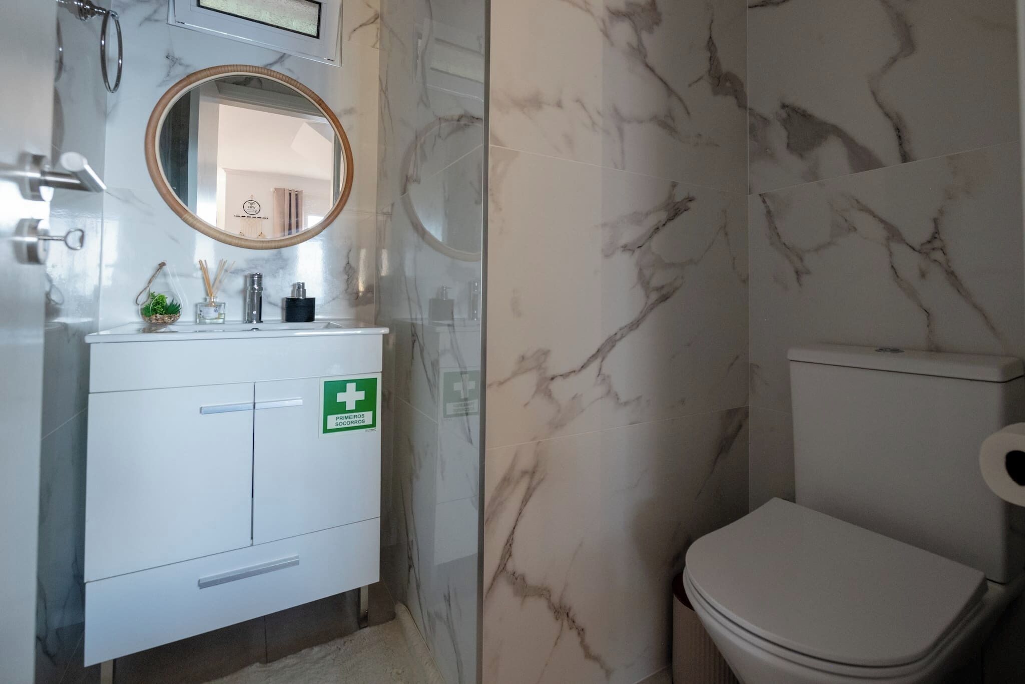A bathroom with a white toilet, a marble wall, a sink with a mirror, and a green emergency sign.