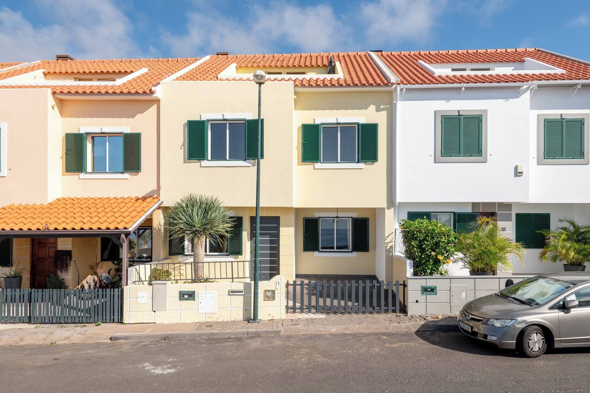 Eine Reihe von Häusern mit Terrakotta-Dachziegeln und grünen Fensterläden, ein verschlossener Eingang und ein geparktes Auto.