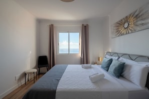 A hotel room with a bed, a chair, a window with curtains, and a wall-mounted artwork. - Ocean View Oasis House (Santa Cruz)