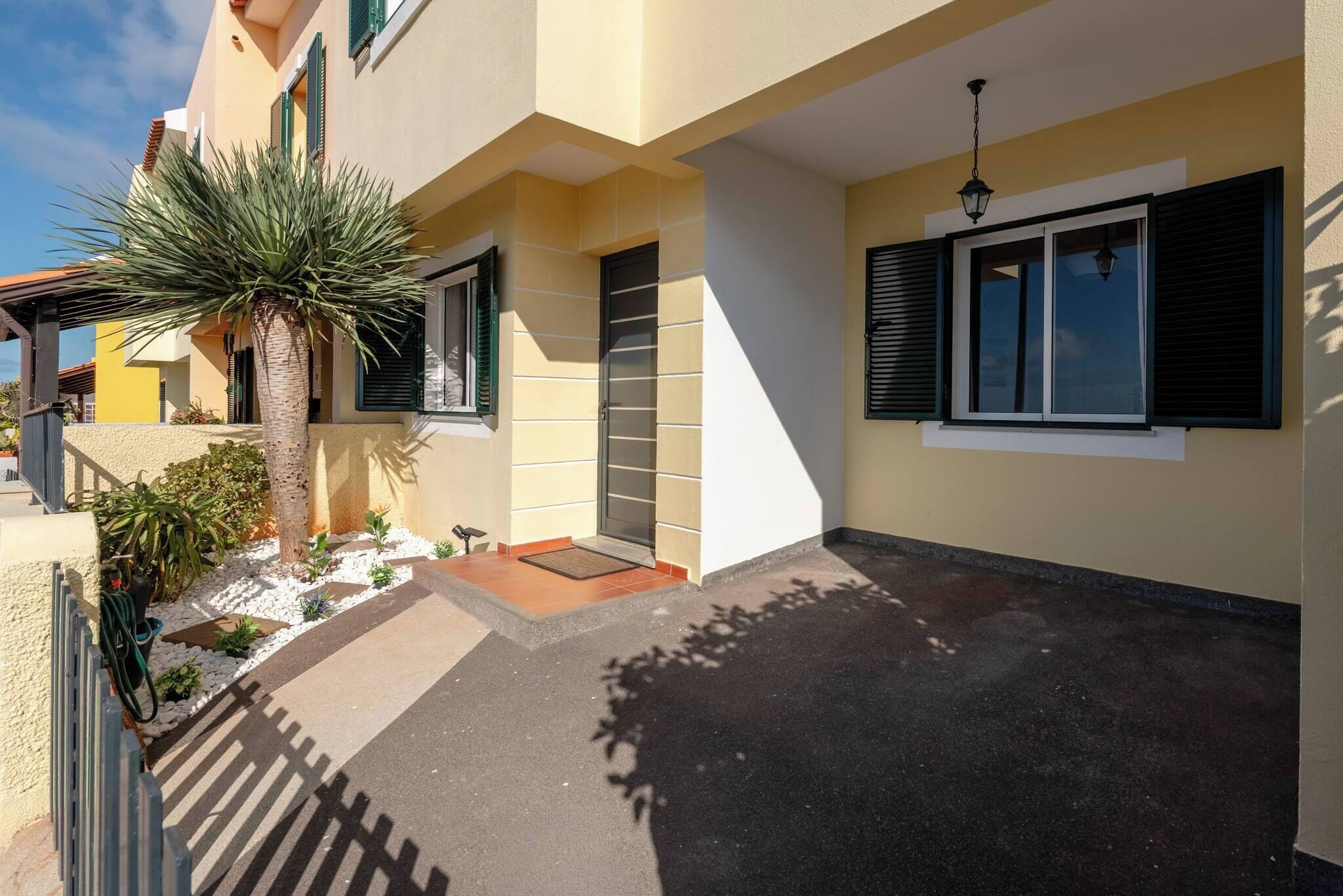 Un edificio residencial con entrada pavimentada, una palmera y una puerta con ventana.